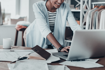 Woman standing over a desk working on a laptop