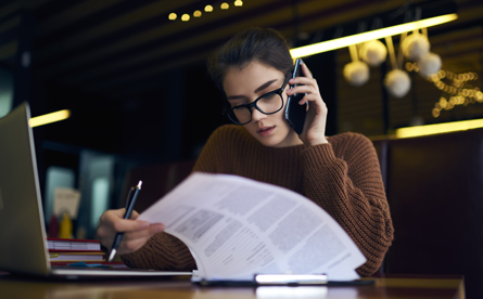 Young woman working on a laptop while on the phone and glancing at paperwork