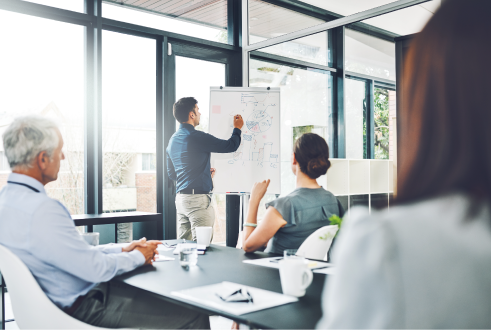 Business team in a meeting watching a man write on a whiteboard