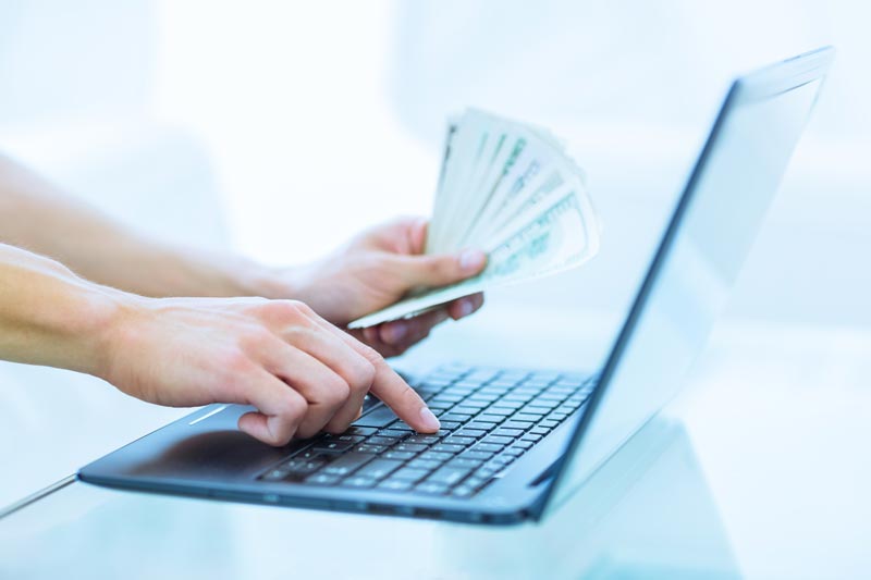 Person holding money while typing on a computer